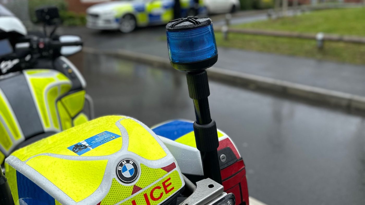 Picture of West Mercia Police bike on the side of a road on a rainy day. The police bike is sat in a housing estate.